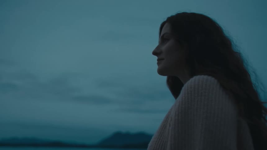 A woman with long dark hair is standing on a beach looking at the water