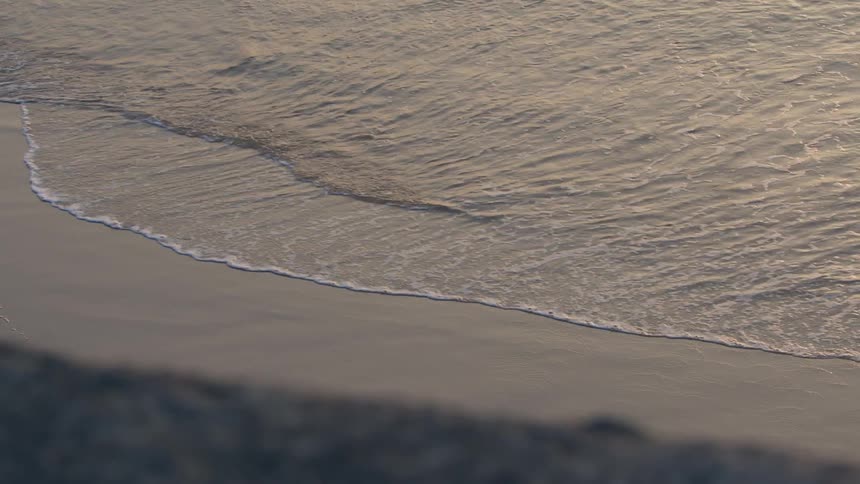 Waves foam as they flow onto sandy beach