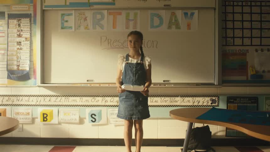 A girl is standing in a classroom holding a paper for her earth day presentation