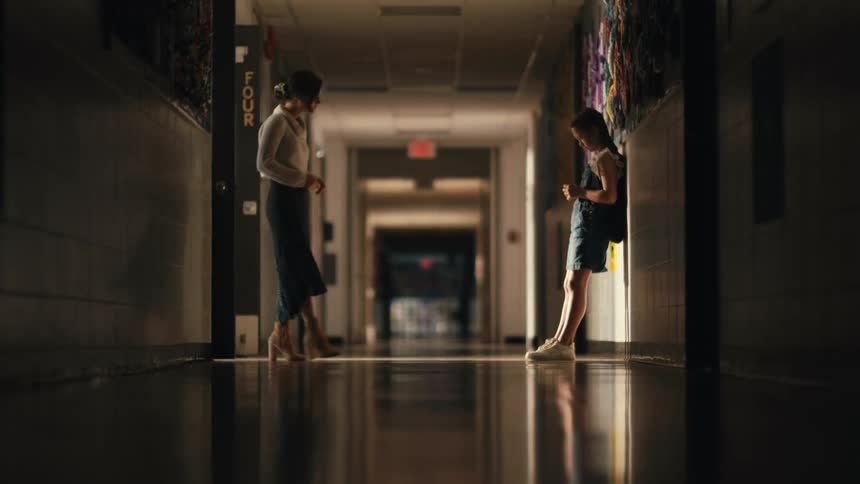 Teacher kneels in front of a student reclined on the hallway in a school