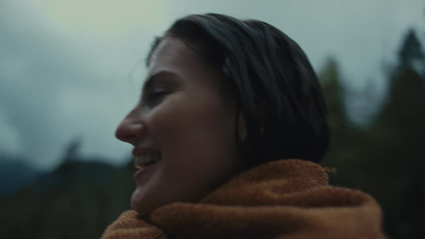 A smiling woman stands outdoors while wrapped in a towel