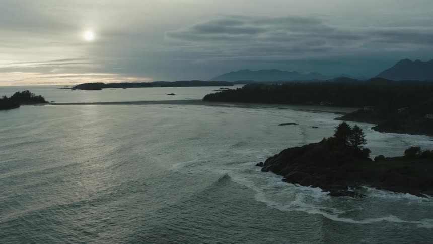 Sun shines onto trees on narrow peninsula as fog obscures mountains on the horizon