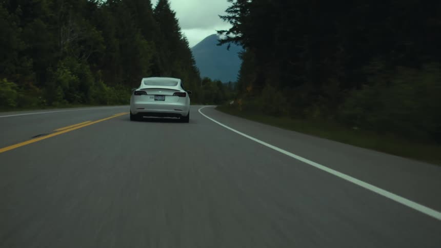 A car is driving on a road in a rural area near mountains