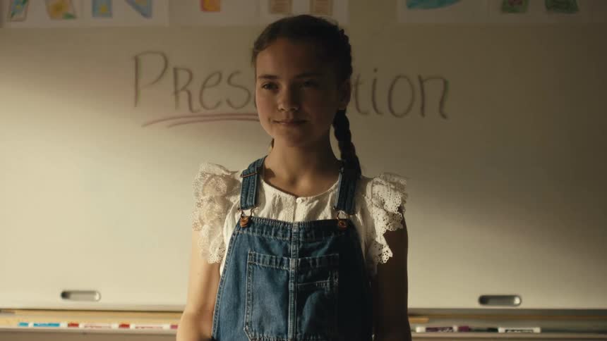 A girl is standing in a classroom and she smiles as she is ready to give her presentation