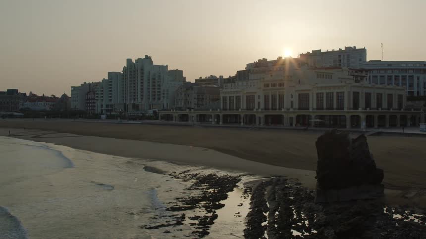 Sun sets over a coastal hotel in front of a beach at sunset