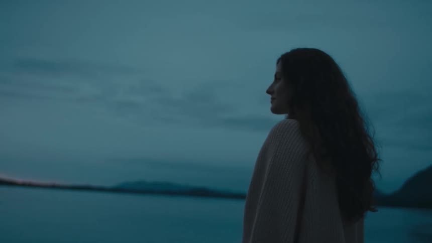 Young woman standing on the coast of a lake looks at the horizon at evening
