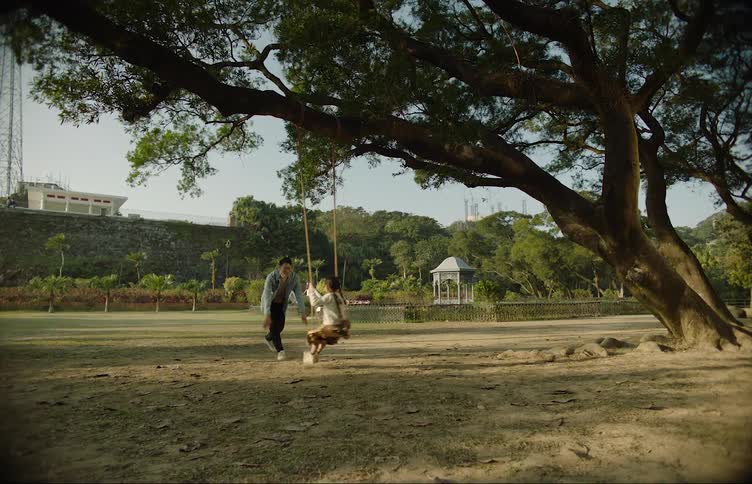 A woman is pushing a little girl on a swing in a neighborhood tree