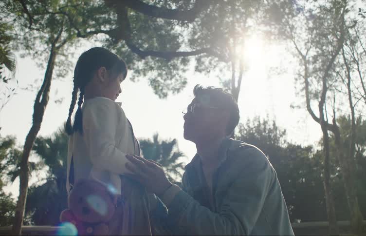 A man tickles his daughter while they stand next to a swing in a park