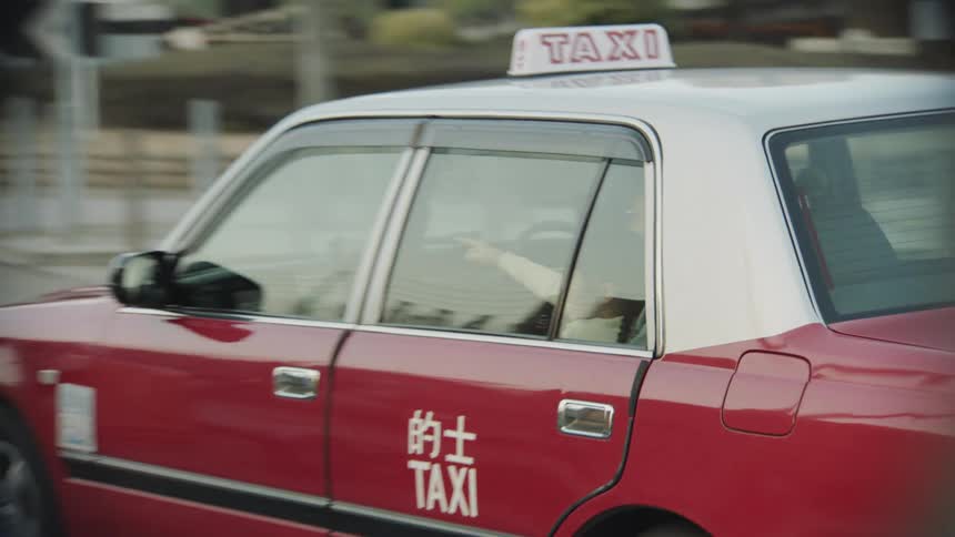 A little girl sitting on her dads lap in the back of a taxi smiles and points as they travel