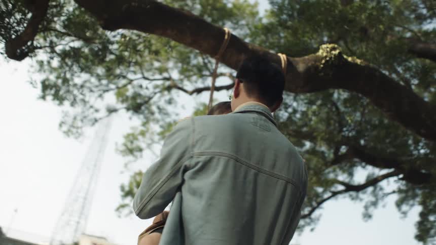 A father carries his daughter around by the swing