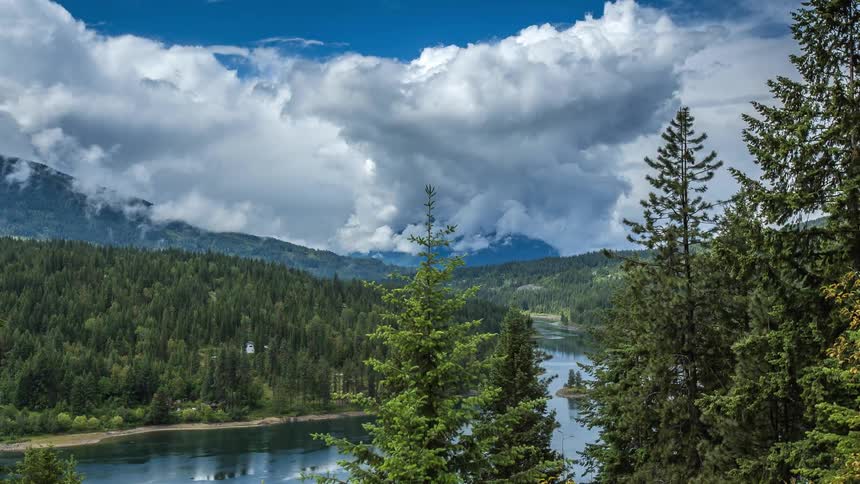 Clouds float over a tree-lined river in the mountains