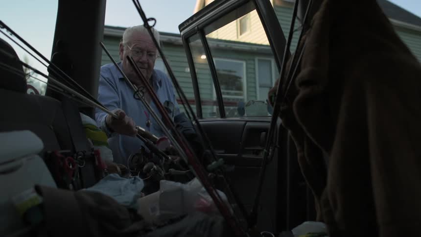 An older man puts fishing poles into a vehicle