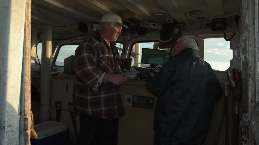 Two men stand in the cabin of a boat talking