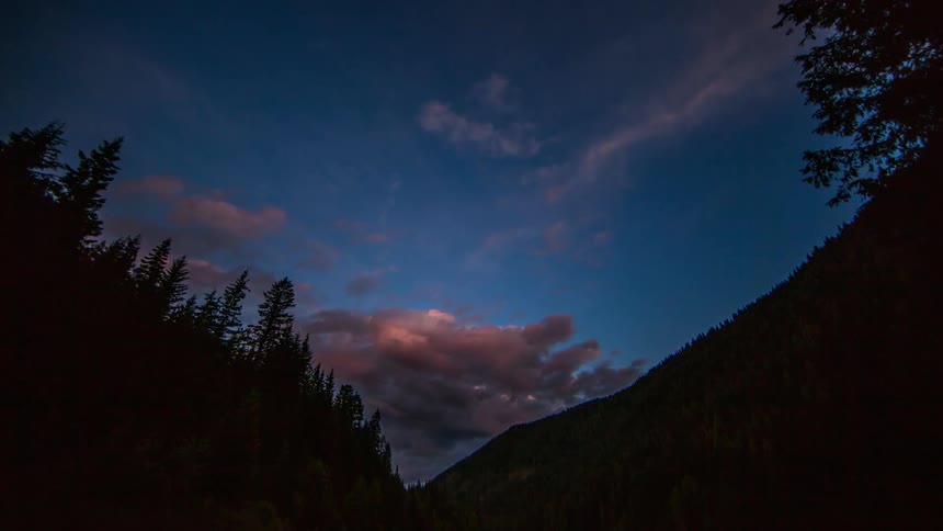 Clouds float over a forested mountainside at dusk