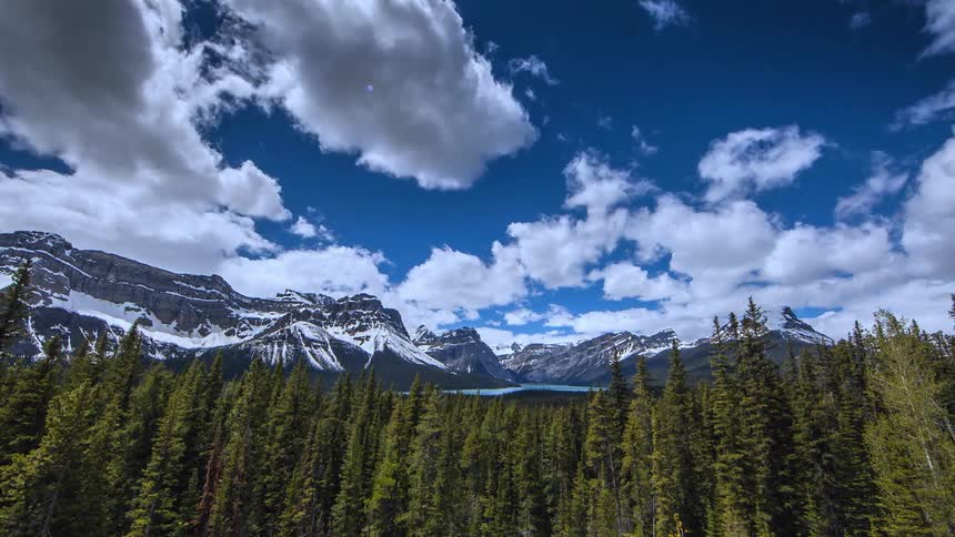 Clouds float over snow-capped mountains and pine trees