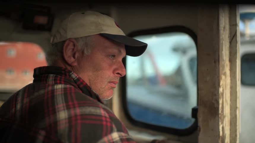 A man is riding in a boat looking out a window from inside the cabin