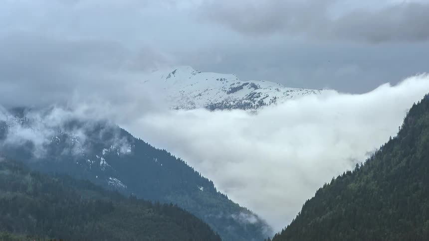 Clouds move around snow and tree covered mountains