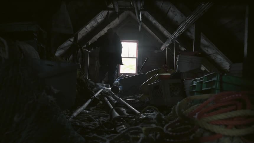 A man is climbing over items in a messy dark room