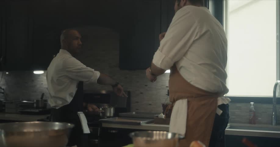 One cook gestures to another as they cook together in a kitchen during the day