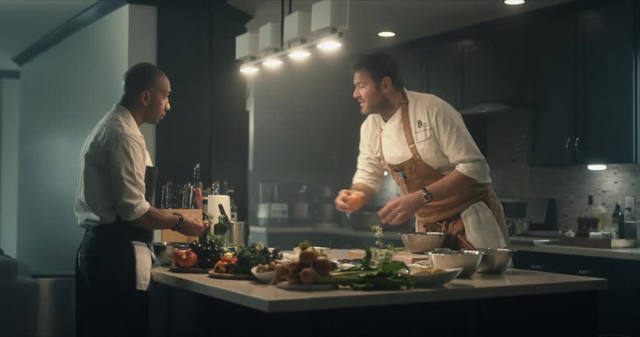 Two male chefs stand at kitchen island prepping