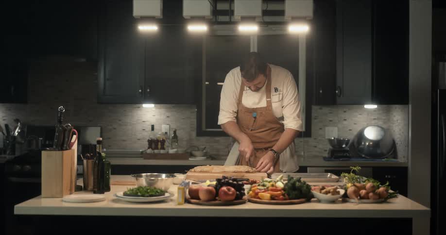 A chef slices food on a wooden cutting board in a kitchen