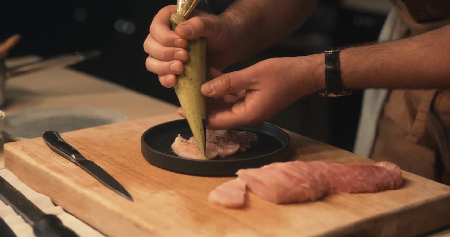 Male chef pipes sauce as garnishment onto plate of fish