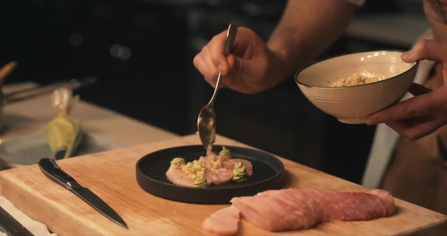 A chef spoons garnish on top of sliced fish