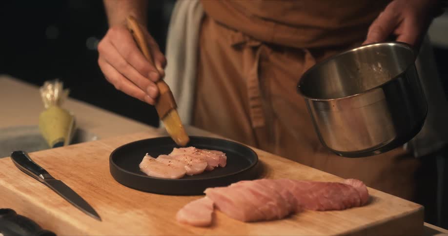 Male chef bastes sliced fish with sauce from pan