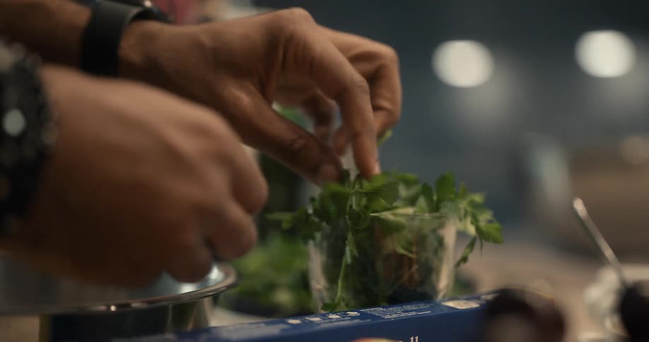 A man is picking herbs from a cup as he is standing over a mixing bowl