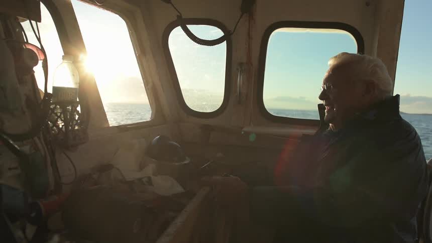 A man is sitting in his boat steering in the water at sunset