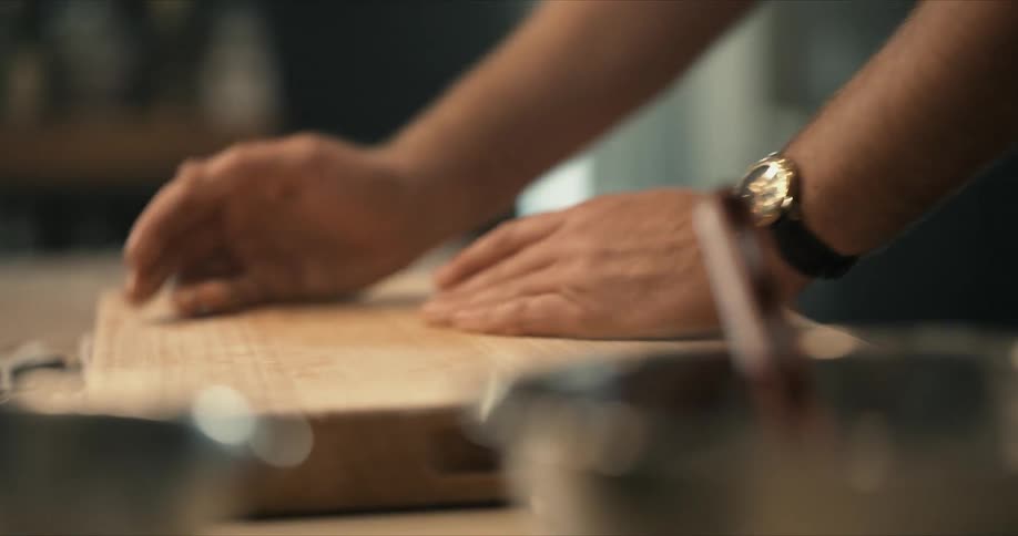 A man is using his hands to clear the flour and crumbs from his cutting board