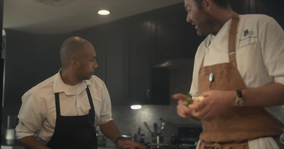 Chef peeling an apple directs another cook toward the stove