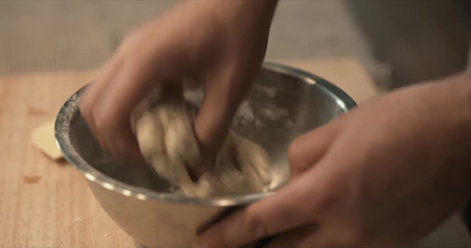 Man hand kneads dough in metal bowl on wooden surface
