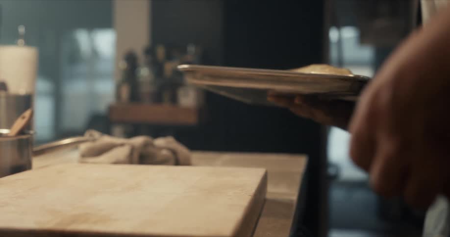 A man picks up a tray with bread dough on it and another man scrapes the cutting board