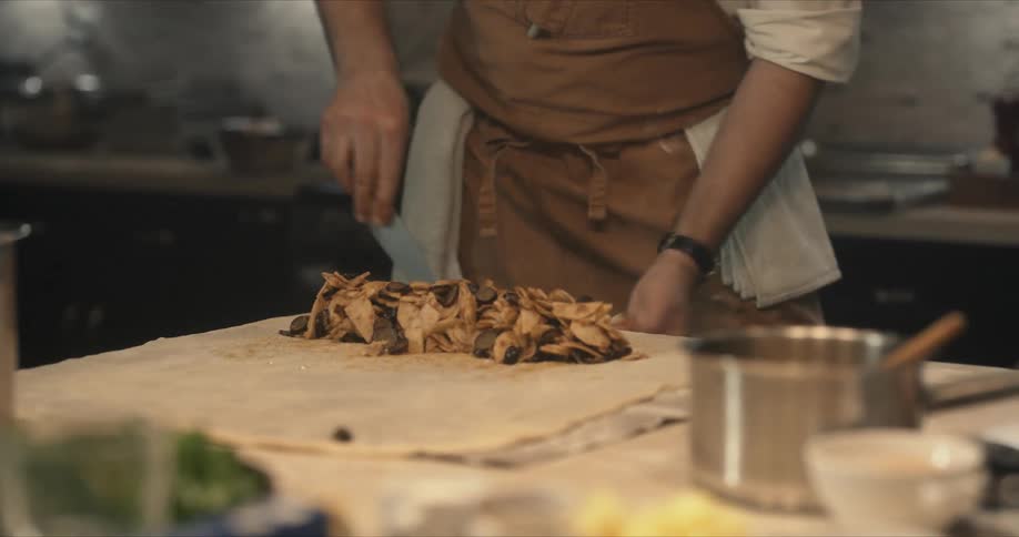 Chef cutting dough to prepare a dish over a table on the dimly lit kitchen