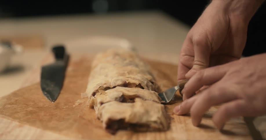 A male chef lifts sliced stuffed pastries from chopping board