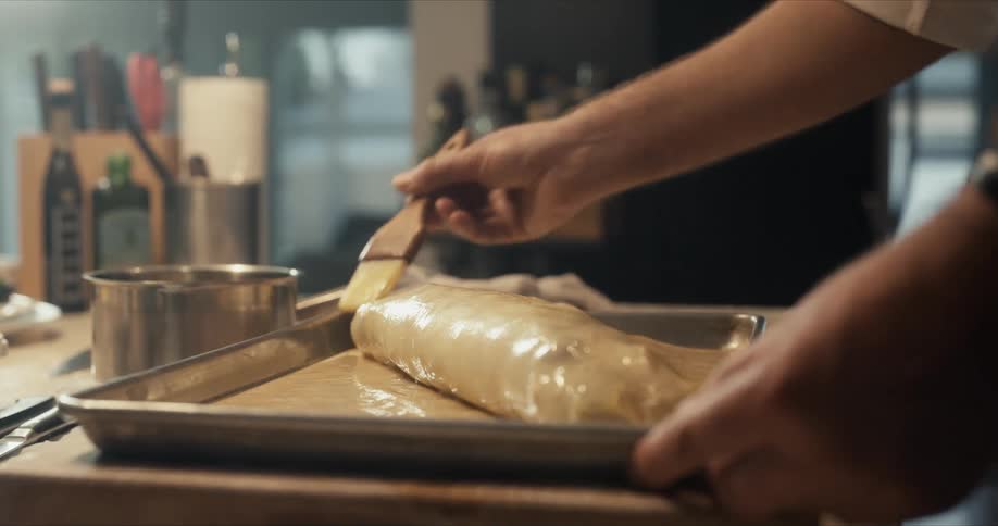 Chef uses a brush to glaze a roll over a tray in the kitchen