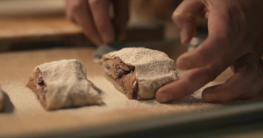 A chefs fingers shake a bit as he carefully lifts food off parchment with a spatula