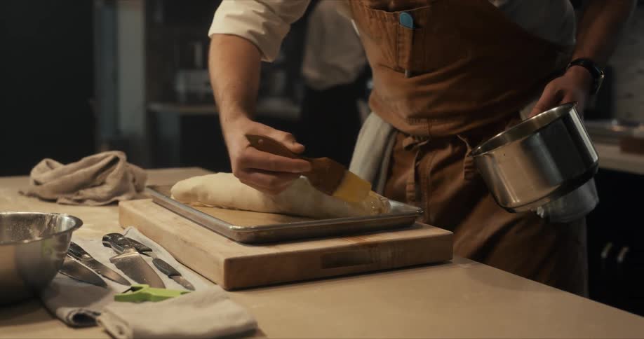 A male brushes a food item with butter or oil in a large kitchen