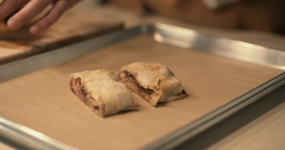 A chef places three slices of apple strudel onto a pan lined with pastry mat