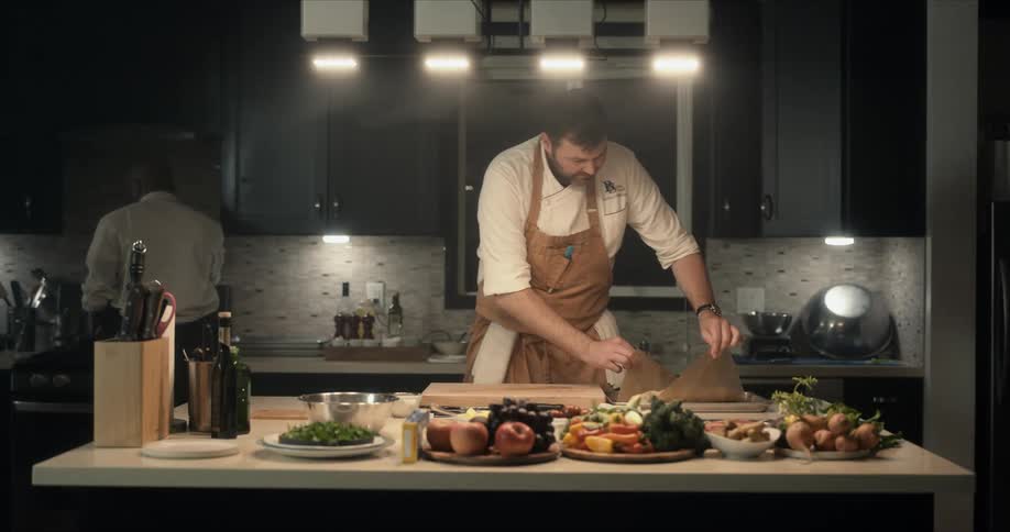 A chef carries a baking pan to a table and moves the contents to a cutting board