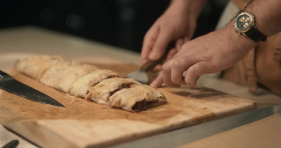 Chef cuts a slice from a loaf using a sharp kitchen knife to place it on a metal tray