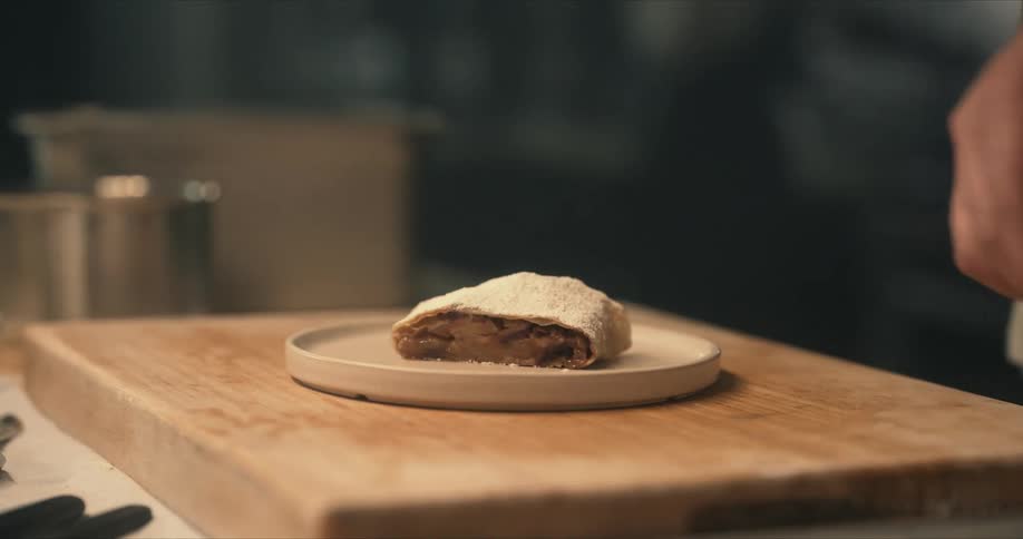 A chef places a slice of fruit pastry on a dish then reaches for a spoon and garnish