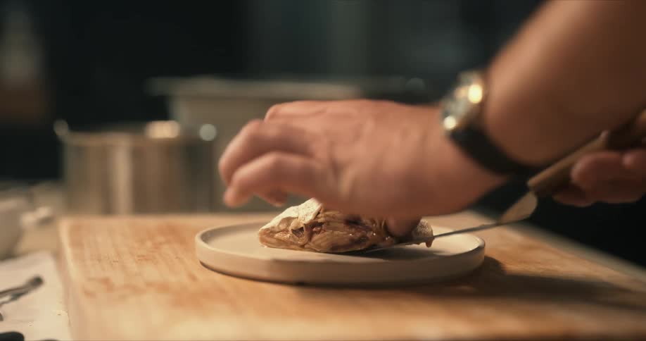 A man plates food using a spatula while standing before a table in a kitchen