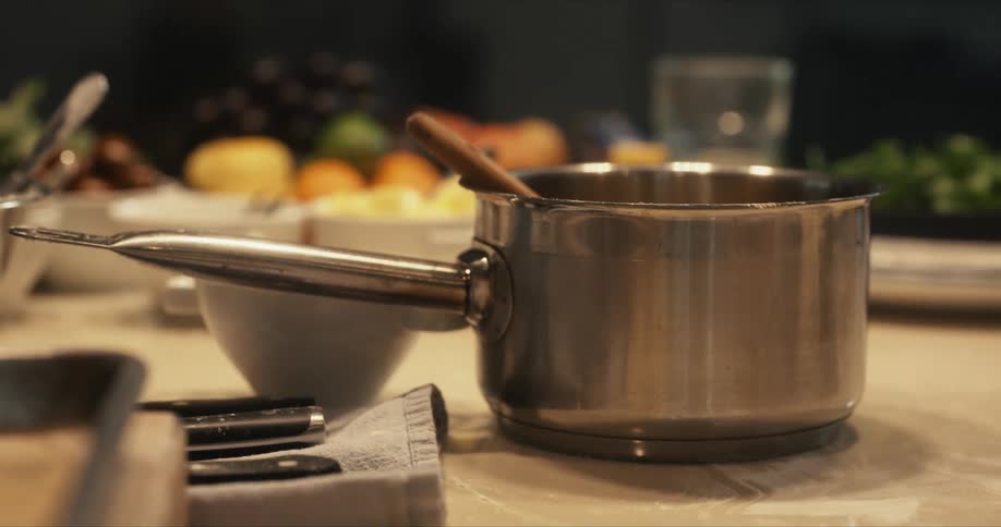 A stainless steel pot sits on a stone island surface near fruit and vegetables