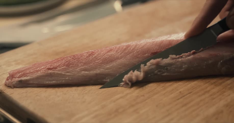 A person carefully cutting raw meat on a wooden cutting board