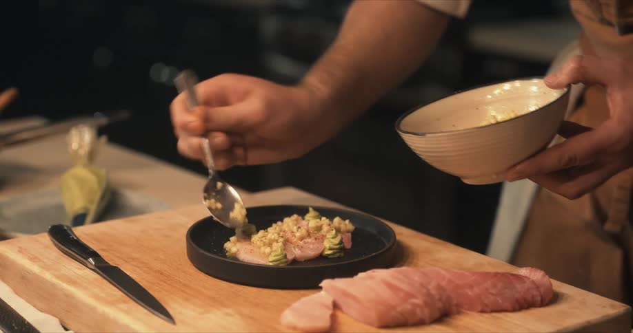 Chef garnishes a dish with sliced garlic on a black dish in the kitchen