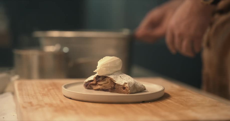 A chef prepares and places a dollop of whip cream on a dessert then hands it off to a waiter