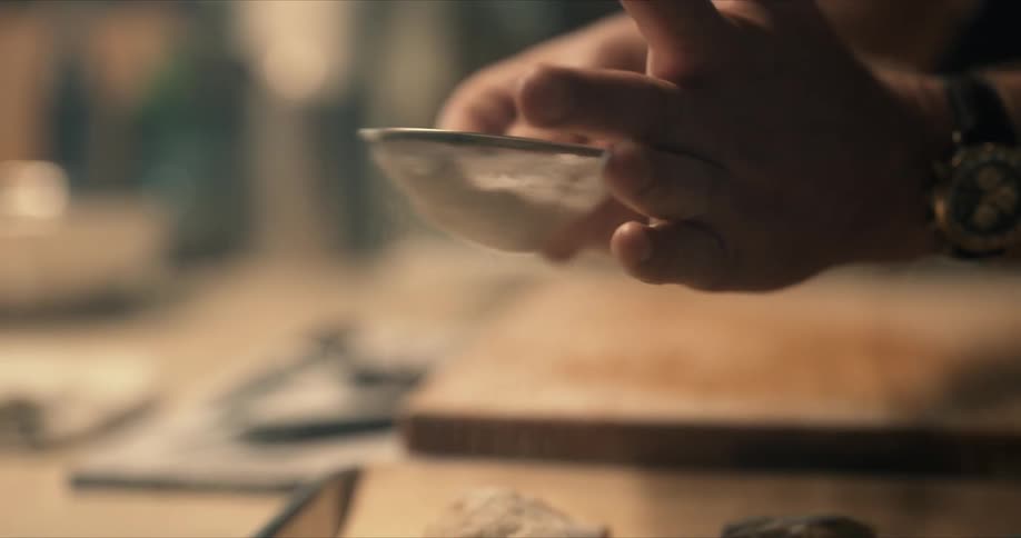A cook shakes powdered sugar from a strainer onto food on the kitchen table