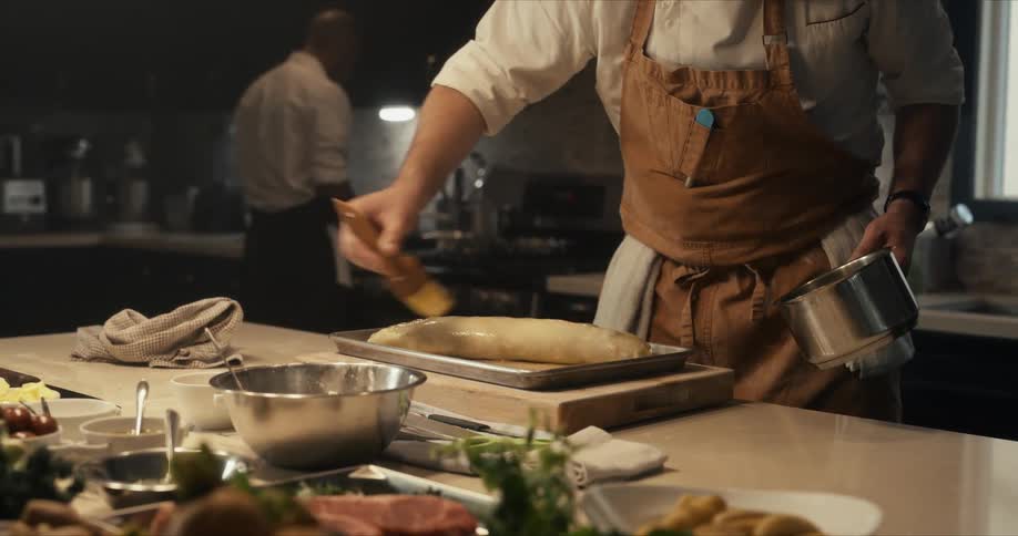A chef brushes melted butter onto a loaf in a pan before baking